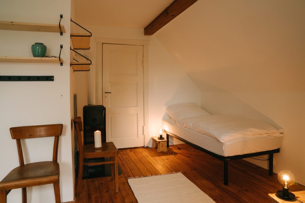 Vierbettzimmer Norden Ausschnitt eines Zimmers mit einem weißbezogenem Bett mit einem Holzstuhl und Regalbrettern ausgestattet