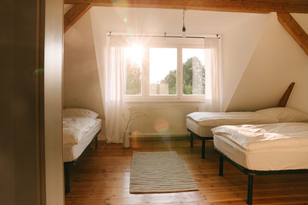 Dreibettzimmer Westen Schlafzimmer mit drei weißbezogenen Betten, durchs Fenster fällt die Sonne herein