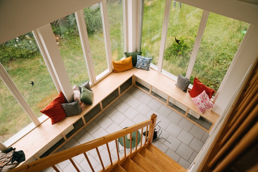 Wintergarten mit Holzbank und bunte Kissen vor großen Fenstern