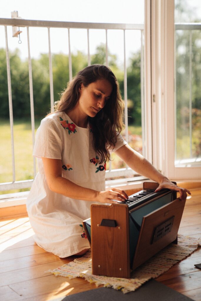 Eine Frau spielt ein Harmonium, im Hintergrund ein Garten