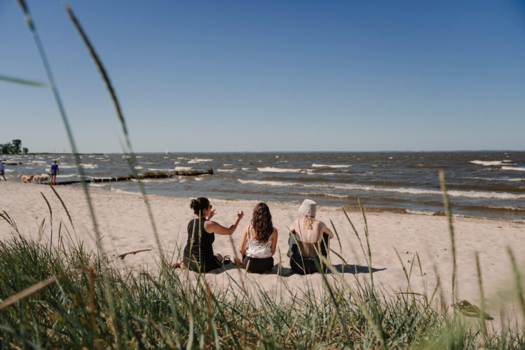 Drei Personen sitzen an einem Strand mit Blick auf das Meer
