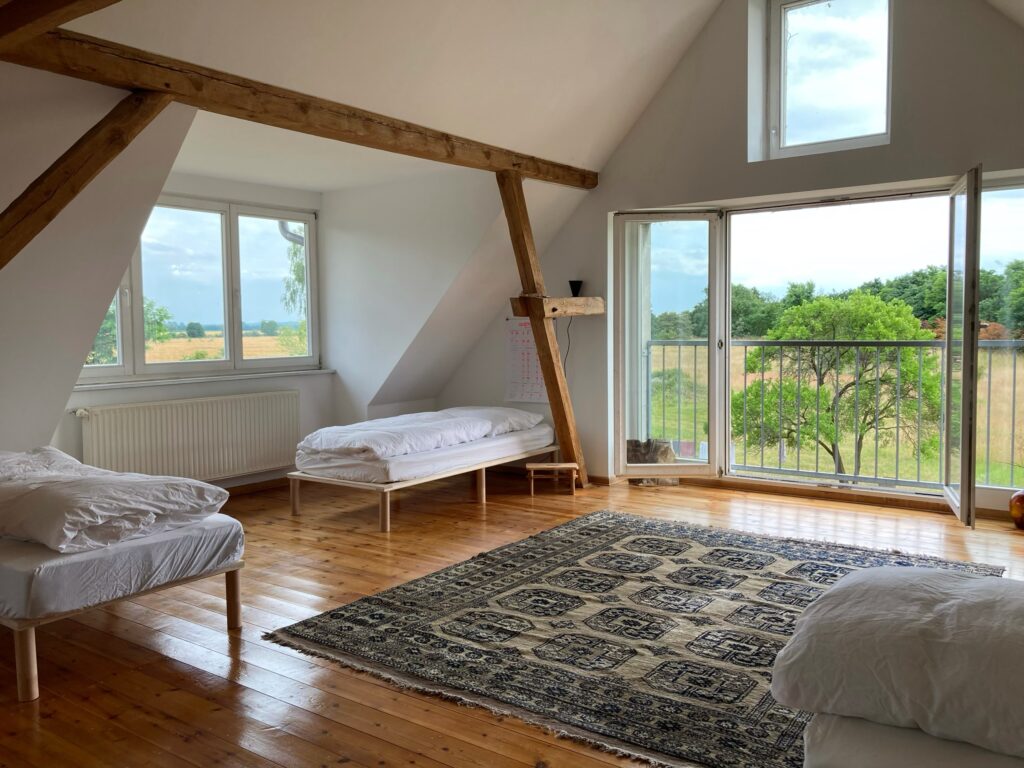 Yogaraum als Schlafsaal umgebaut mit tollem Ausblick Großer Raum mit vielen Fenstern und Blick ins grüne mit mehreren Betten und einem Teppich ausgestattet